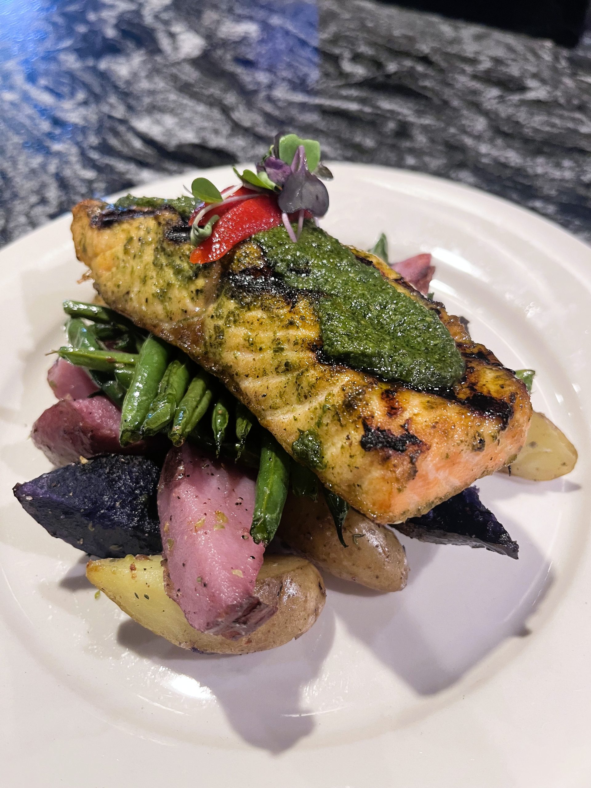 Grilled salmon with pesto, green beans, and roasted potatoes on a white plate.
