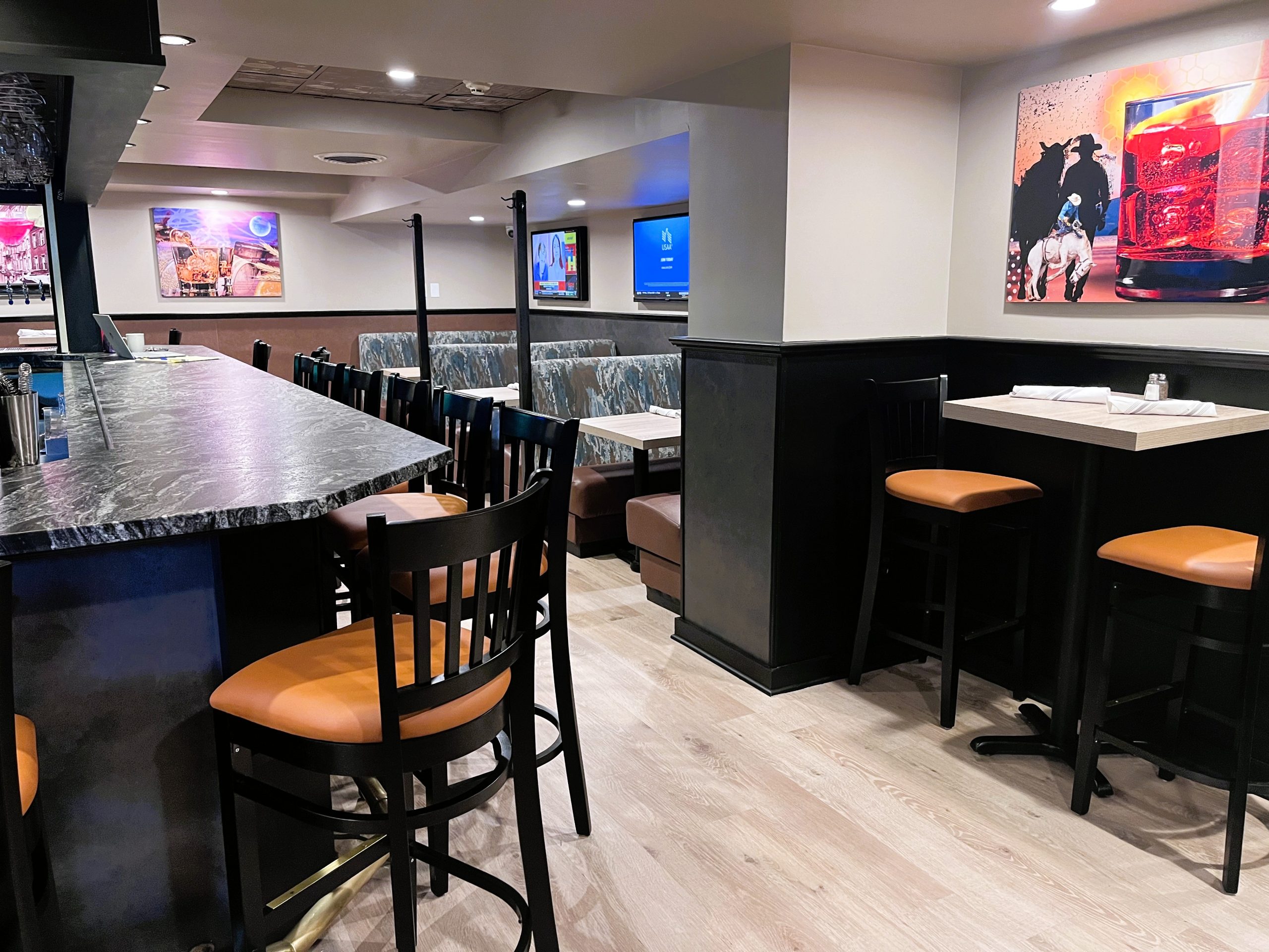 A modern restaurant interior with a bar counter, high chairs, booth seating, and wall art.